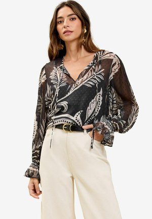 Sort gennemsigtig bluse med hvide paisley- og polka dot-mønstre; har V-hals, snore og flæser på lange ærmer.