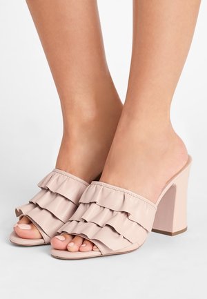 Jasnoróżowe, otwarte klapki na obcasie z trzema falbankami na górze. Wykonane z gładkiej skóry, z obcasem typu blok.
