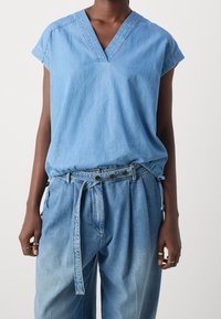 Lyseblå denimtop med korte ærmer og V-hals, parret med løstsiddende blå denimbukser med et bundet bælte og to frontlommer.