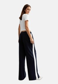 Navy wijde broek met witte zijstreep, voorzien van een elastische tailleband en zachte stof. Gecombineerd met een cropped witte t-shirt.