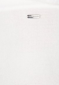 Țesătură albă cu dungi, cu un finisaj texturat și detalii din metal de culoare argintie, incluzând un etichetă metalică branduită.