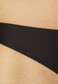 Bas de bikini noir en tissu lisse. Caractérisé par un design minimaliste avec une coupe taille basse. Doublure intérieure texturée visible.