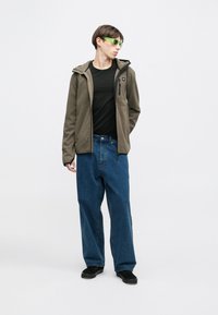 Ελαιόχρωμο φλις μπουφάν με κουκούλα, μαύρο μπλουζάκι, φαρδιά μπλε τζιν και μαύρα παπούτσια. Τα πράσινα γυαλιά ηλίου ολοκληρώνουν το σύνολο.