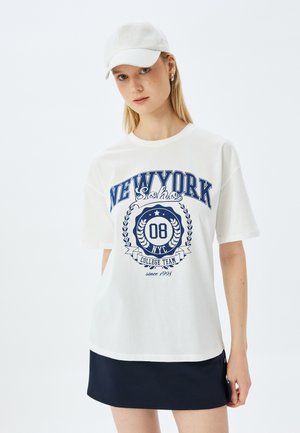 T-shirt en coton blanc avec texte imprimé en bleu marine "NEW YORK 08 NYC COLLEGE TEAM" accompagné d'un design de laurier. Assorti à une jupe sombre.