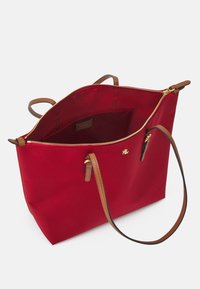 Czerwona torba materiałowa z brązowymi skórzanymi uchwytami i akcentami. Posiada złoty zamek błyskawiczny i wewnętrzną kieszeń. Prosta, zorganizowana forma.