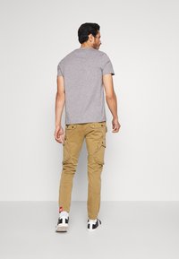 Camiseta gris de manga corta combinada con pantalones cargo color caqui que cuentan con bolsillos laterales y un ajuste entallado, completados con zapatillas en negro y blanco.