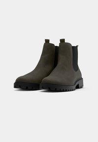 Olivengrüne Chelsea-Boots mit glattem Obermaterial, schwarzen elastischen Seitenteilen und einer strukturierten schwarzen Gummisohle. Mit Zuglaschen für ein einfaches Anziehen.
