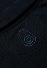 Marinblå polo t-shirt med texturerat tyg, med en blå broderad logotyp på bröstet som föreställer en cirkulär design.