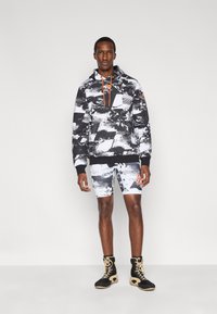 Ασπρόμαυρο hoodie με αφηρημένο σχέδιο και πορτοκαλί λεπτομέρειες, σε συνδυασμό με ταιριαστό σορτς. Φορεμένο με μαύρα μποτάκια με κοψίματα.