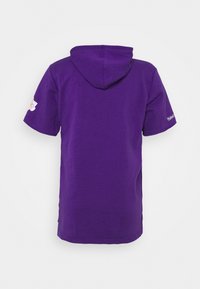 Felpa corta viola con maniche a sbuffo, logo dei Los Angeles Lakers sulla manica sinistra e testo Mitchell & Ness sulla manica destra, vista da dietro.