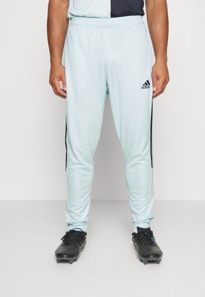 Pantalones deportivos de color azul claro con rayas laterales negras y cinturilla elástica, combinados con zapatos de fútbol negros. El material parece suave y elástico.