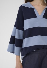 Pulover tricotat cu dungi în nuanțe de bleumarin și albastru deschis, cu decolteu în V și guler, având mâneci late și o croială lejeră. Textură netedă.