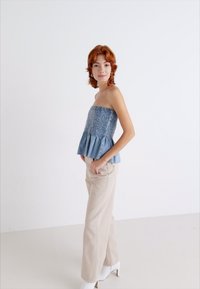 Svijetloplavi strapless peplum top s naboranom teksturom, uparen s kremastim hlačama širokih nogavica i bijelim potpeticama na jednobojnoj pozadini.