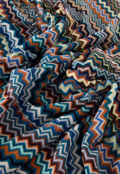 Strikket stoff med flerfarget sikksakkmønster i blågrønn, oransje, brun, blå og krem, vist med myke folder og tekstur.