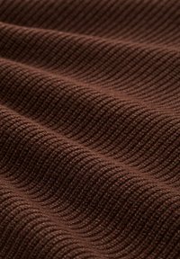 Brauner gerippter Stoff mit einer strukturierten Oberfläche und wellenförmigem Muster, das unterschiedliche Tiefen und Schatten über den Falten zeigt.