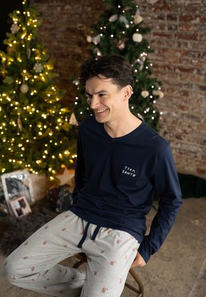 Navy long-sleeve pajama top with "TEAM SANTA" embroidery; light gray bottoms featuring red gingerbread man patterns. Warm, relaxed fit.