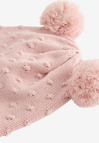 Bonnet en tricot rose avec deux grands pompons moelleux sur le dessus. Présente un motif texturé avec de petites bosses sur l'ensemble du tissu.