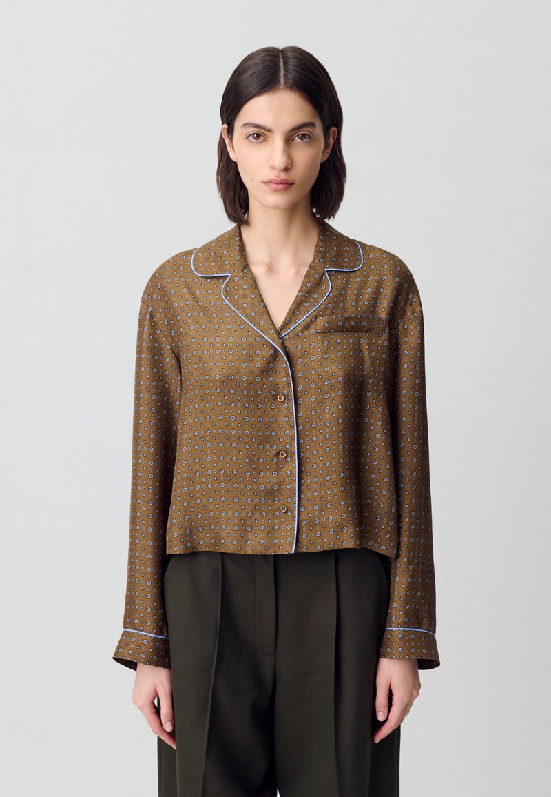 Camicia marrone a fantasia con bordo blu, chiusura a bottoni e maniche lunghe, dotata di tasca sul lato sinistro del petto.
