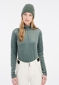Haut à manches longues avec col zippé en vert atténué, orné d'un motif en tricot à câbles texturé, associé à un pantalon crème comportant deux boutons et des poches latérales.