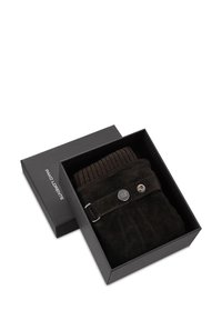 Ciemnobrązowe zamszowe spodnie starannie złożone z ryflowanym, dzianinowym pasem, wyeksponowane w czarnym firmowym pudełku z akcentem w postaci srebrnego guzika.