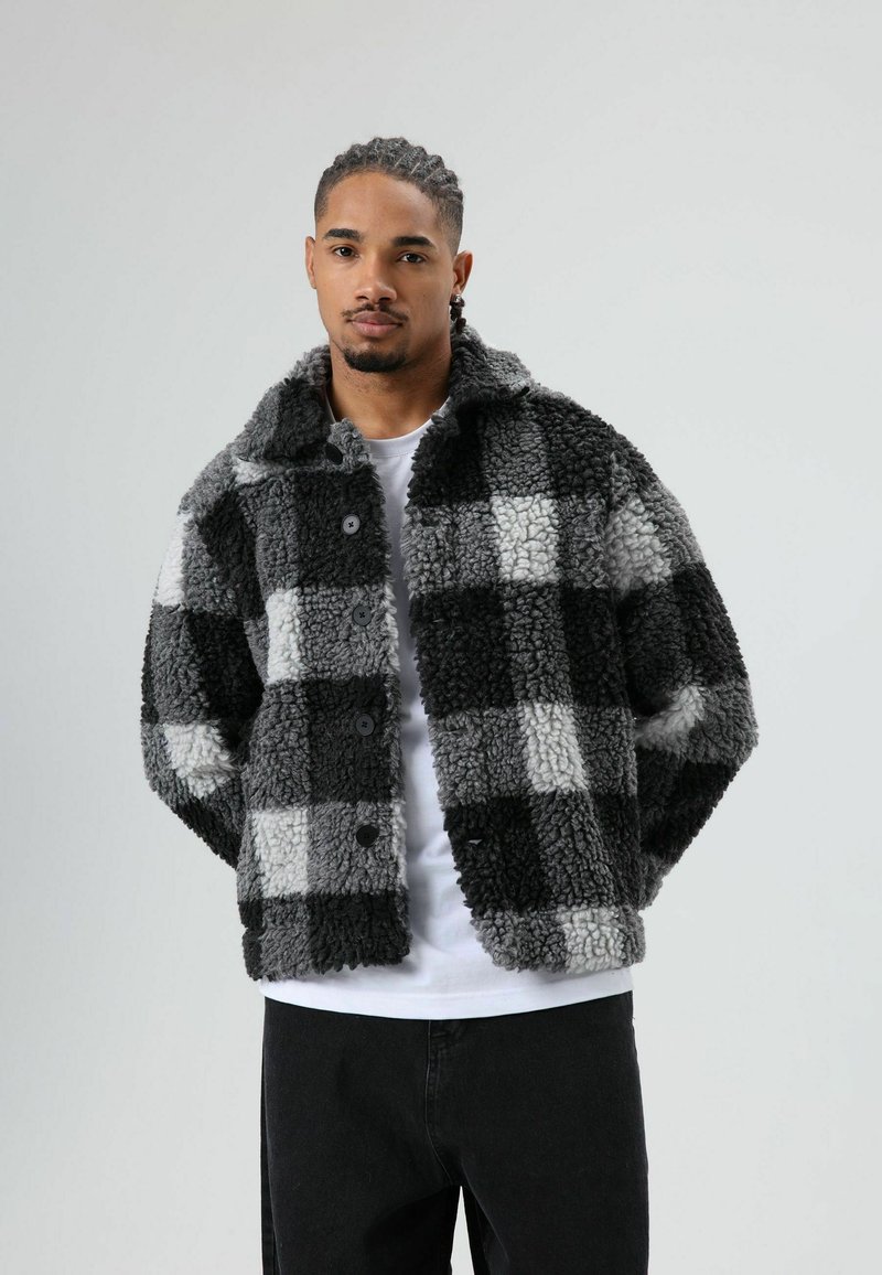 Zwart en grijs geruit jack gemaakt van gestructureerde nep bont, met een kraag en knoopsluiting, gedragen over een wit overhemd.