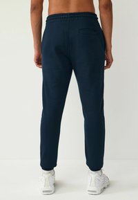 Pantalones jogger de color azul oscuro con una textura suave, cinturilla elástica y un solo bolsillo trasero. Combinados con zapatillas blancas.