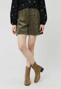 Shorts en velours côtelé vert olive avec des plis, associés à des bottines en suedine marron. L'ensemble est composé d'un haut à manches longues noir à motifs floraux.