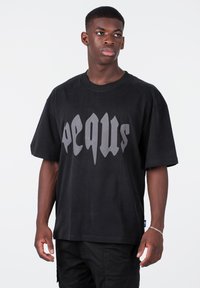 Černé oversized tričko vyrobené z bavlny s velkým šedým grafickým potiskem. Krátké rukávy a design s kulatým výstřihem.