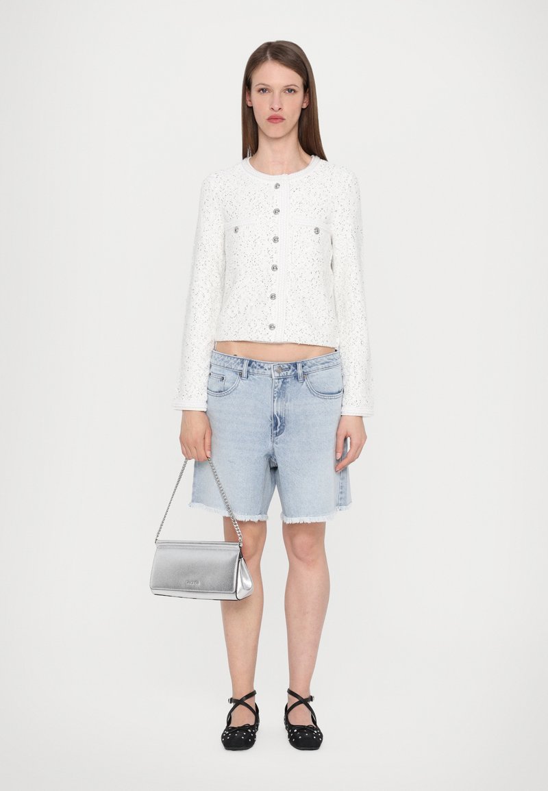 White speckled cropped jacket with silver buttons, paired with light blue denim shorts and black polka dot flats. Silver chain handbag.