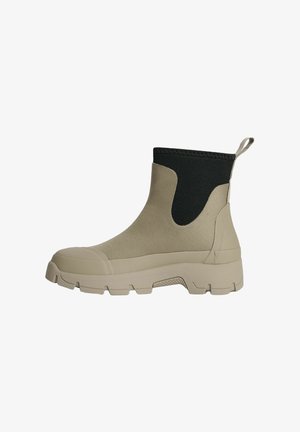 Beige ankelstøvle med tyk, mønstret sål og sort elastisk øvre krave med træk-flig ved hælen.