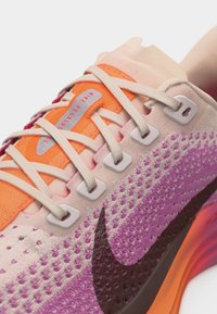 Κοντινό πλάνο αθλητικού παπουτσιού Nike Pegasus σε αποχρώσεις ρόζ, πορτοκαλί και μοβ, με λευκά κορδόνια και μαύρο λογότυπο Nike.