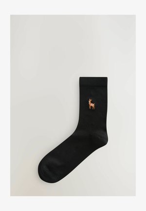 Chaussette en coton noire avec un haut côtelé, présentant un petit motif de cerf brodé en orange et blanc sur le côté extérieur.