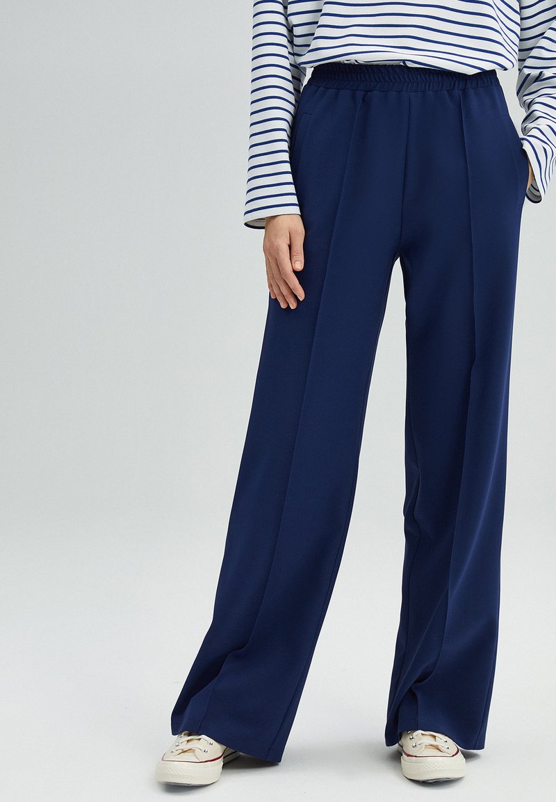 Navy wide-leg trousers made of lightweight fabric with an elastic waistband and side pockets, paired with a striped long-sleeve top.