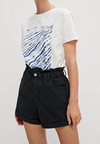 T-shirt blanc avec un graphique à rayures bleues, associé à un short navy foncé avec une taille froncée et un ourlet roulé.