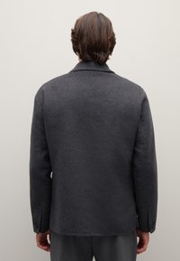 Dunkelgrauer Wollmischmantel mit Kerbkragen, strukturierter Oberfläche, Knopfakzenten an den Manschetten und einer taillierten Passform. Rückansicht zeigt saubere Nähte.