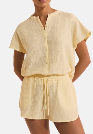 Donna che indossa una maglietta a maniche corte con bottoni, di colore giallo chiaro e texture, e pantaloncini abbinati con vita elastica e coulisse.