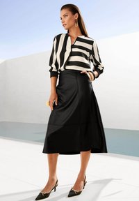 Zwarte leren knie-lange rok met een aansluitende taille, gecombineerd met een witte blouse met gedurfde zwarte strepen. Inclusief puntige zwarte hakken.