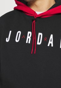 Felpa nera con cappuccio e lacci rossi, caratterizzata dal logo "JORDAN" ricamato in bianco, con la lettera "A" in rosso. Texture morbida.