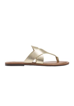 Płaski sandał z brązową podeszwą i metalicznymi złotymi krzyżującymi się paskami z pętlą na palec, widziany z boku na białym tle.