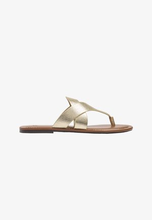 Płaski sandał z brązową podeszwą i metalicznymi złotymi krzyżującymi się paskami z pętlą na palec, widziany z boku na białym tle.