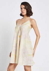 Cremefarbenes A-Linien-Kleid mit V-Ausschnitt und dünnen Trägern, das lila Blumen- und Schriftmuster aufweist. Leichter Stoff mit lockerer Passform.
