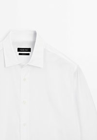 Chemise blanche à boutons avec col pointu, étiquette de marque visible "Massimo Dutti" à l'intérieur, présentée sur un fond blanc uni.