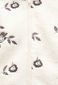 Kremasta majica od runa s prednjim patentnim zatvaračem, ukrašena tamnim cvjetnim vezom i listovima, mekom teksturom i minimalističkim dizajnerskim elementima.