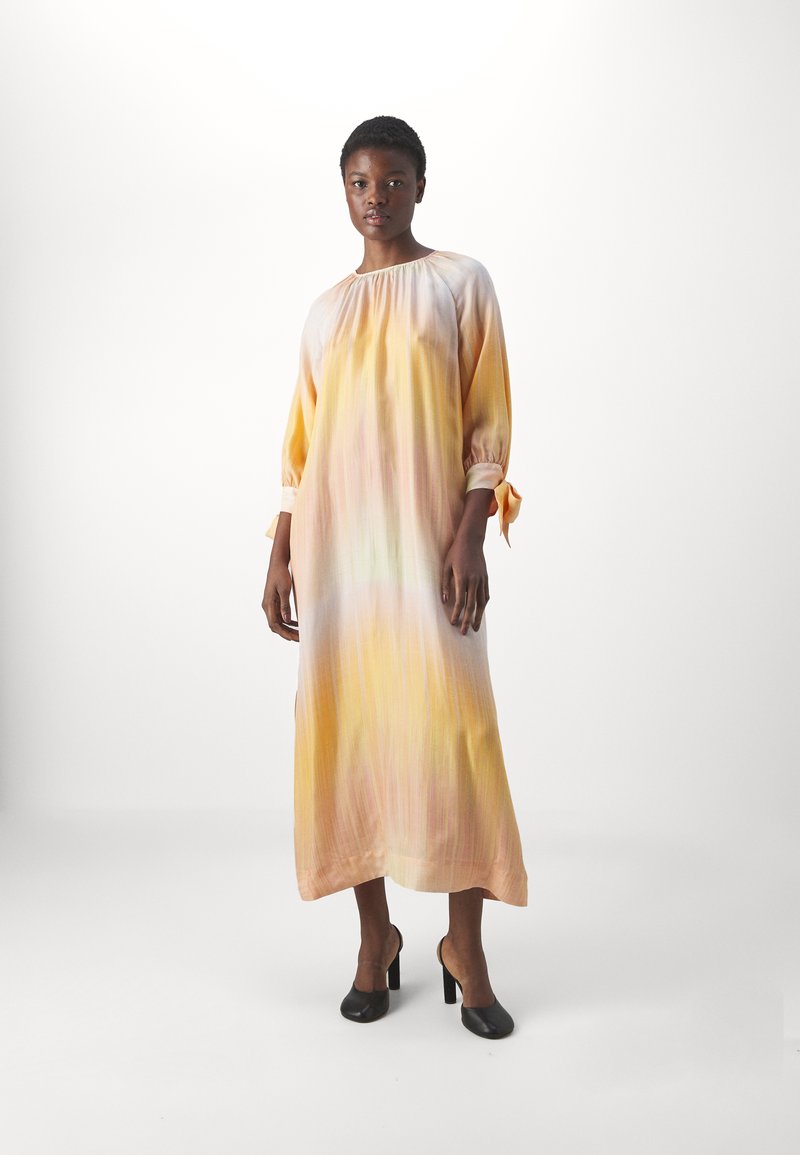 Robe longue et fluide en dégradé de jaune et de rose, fabriquée en tissu léger. Présente un décolleté froncé et des manches nouées.