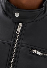 Veste de moto en cuir noir avec un col haut, des fermetures éclair argentées et des détails à boutons-pression, dotée de coutures horizontales distinctes.