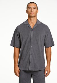 Camisa de botones de manga corta en gris, con una textura suave y un cuello, que presenta botones morados y un ajuste ligeramente holgado.