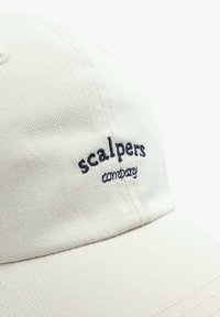 Beige cotton baseball cap with a curved brim; features blue embroidered text "scalpers" and "company" on the front. Textured fabric.