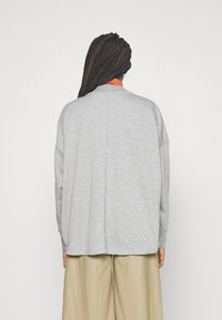 Grå oversized sweatshirt med sänkta axlar, ribbad halsringning och en slät yta. Bärs över beige vida byxor.
