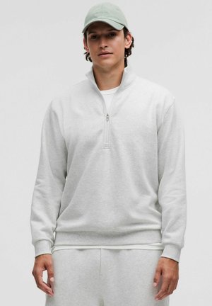 Light gray zip-up sweatshirt with long sleeves, soft texture, and ribbed cuffs. Worn over a white shirt, paired with matching pants.