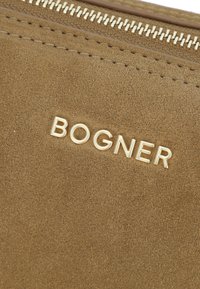 Porta trucco in suede color miele con zip dorata e logo "BOGNER" impresso sul davanti, caratterizzato da una texture liscia e minimali decorazioni.